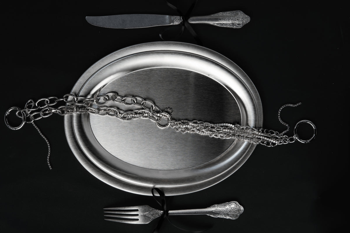 Still life of MUTED WHITE silver chains laid on a silver platter with antique cutlery